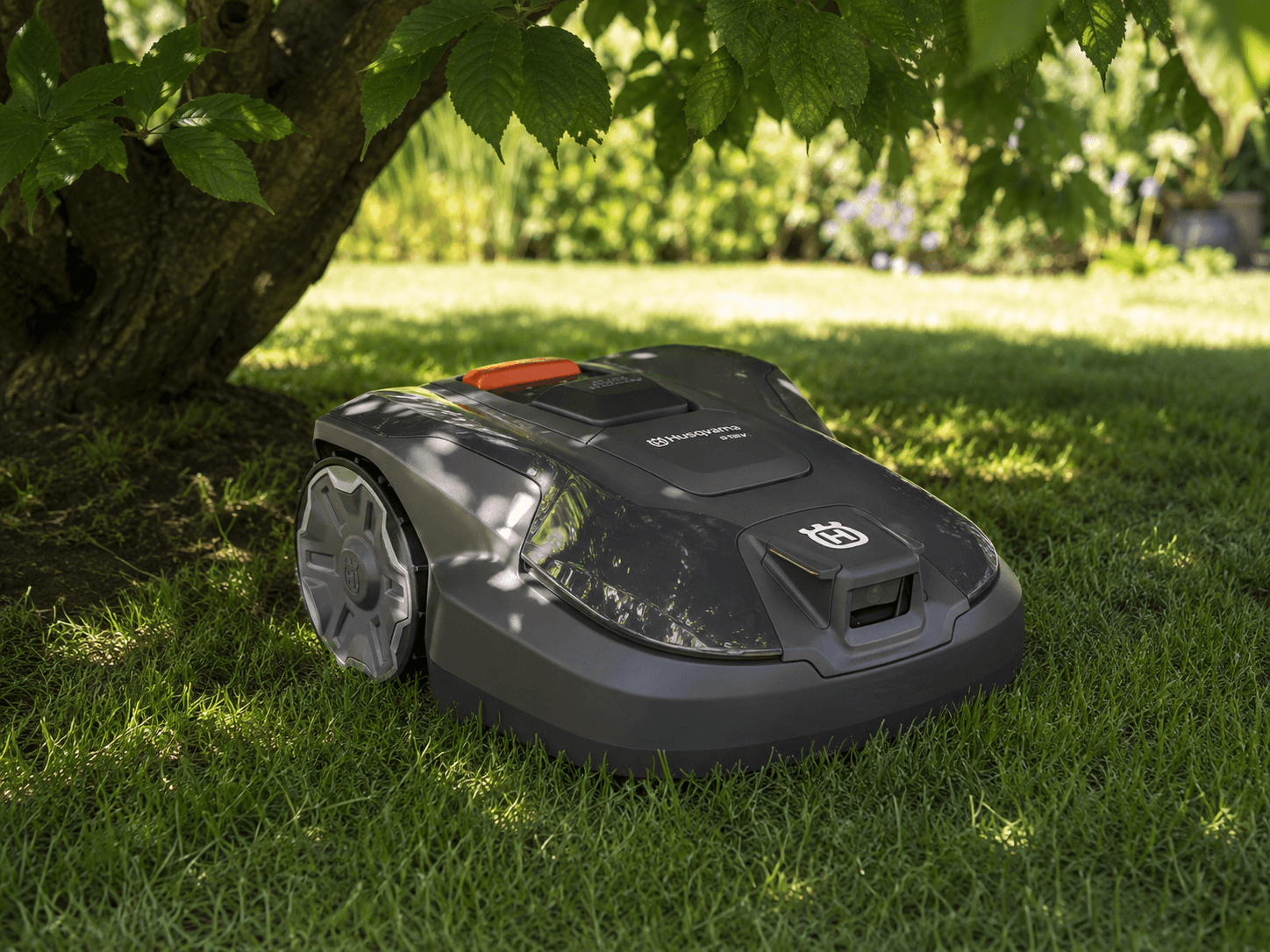 Husqvarna RTK robotic mower drives in the shade under a tree on well-kept lawn.